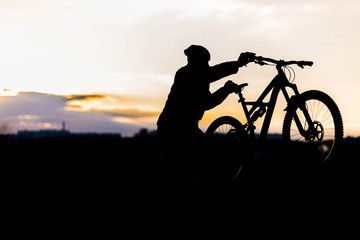 Fototapeta na wymiar Mountain biker standing on top of a mountain with a bicycle, a beautiful sunset. Silhouette of a cyclist.