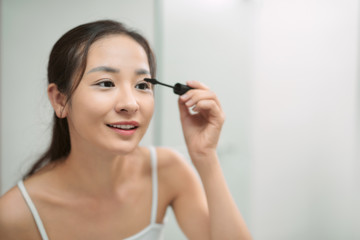 Young asian woman applying mascara in bathroom