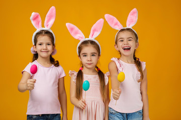 happy cute little child girls with pink bunny ears holding painted Easter eggs on studio yellow background. Easter day