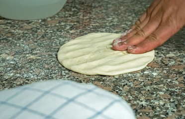 A chef rolls and flattens naan bread dough on a kitchen work top.