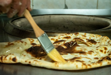 A freshly baked Tandoori cooked Naan bread is brushed with melted butter on a kitchen work top surface.