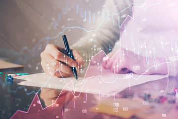 Hand taking notes in notepad. Forex chart holograms in front. Concept of research. Multi exposure