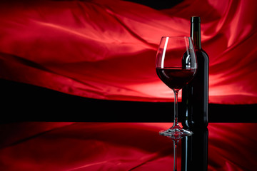 Wineglass and bottle of red wine on a black reflective background.