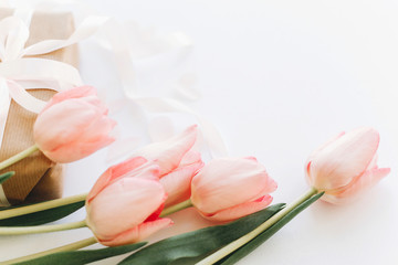 Fototapeta premium Happy womens day. Pink tulips and gift box with ribbon on white background. Stylish tender image. Greeting card with space for text. Happy Mothers day. Wedding or valentine celebration
