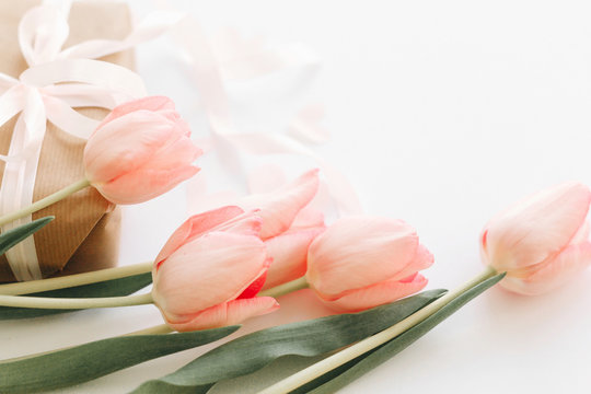 Happy Mothers day. Pink tulips with ribbon on white background with gift box. Stylish tender image. Happy womens day. Greeting card with space for text.  Wedding or valentine celebration