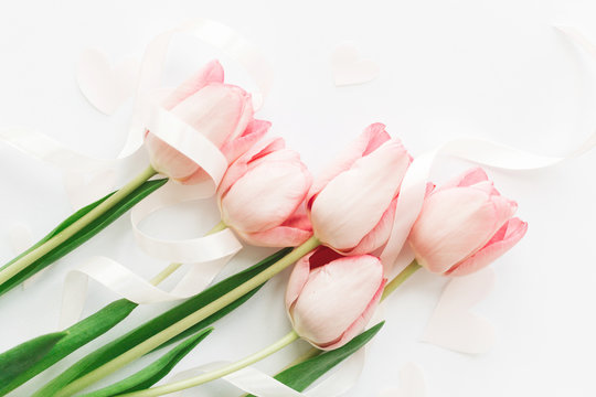 Happy Mothers day. Pink tulips with ribbon and hearts on white background, flat lay. Stylish soft spring image. Happy womens day. Greeting card mockup.   Hello spring