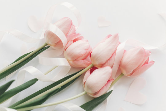 Pink tulips with ribbon and hearts on white background, flat lay. Stylish soft spring image. Happy womens day. Greeting card mockup. Happy Mothers day.  Hello spring