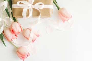 Pink tulips flat lay with ribbon and gift box on white background, space for text. Stylish soft image. Happy womens day. Greeting card mockup. Happy Mothers day. Hello spring