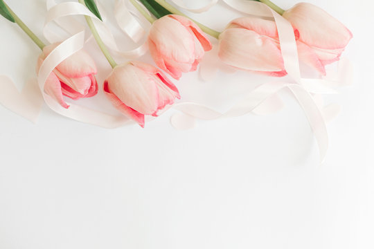Happy Mothers day. Pink tulips with ribbon and hearts on white background, flat lay. Stylish soft spring image. Happy womens day. Greeting card mockup with space for text.  Hello spring
