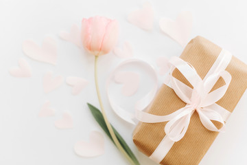 Obraz na płótnie Canvas Gift box with ribbon and pink tulip flat lay on white background, space for text. Stylish soft spring image. Happy womens day. Greeting card mockup. Happy Mothers day. Romantic Valentines day