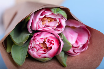 A bouquet of three tulips in a paper wrapper lies on a table. Close up view.