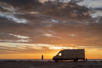 sunset / sunrise at rocky seaside with travel trailer. Dramatic and calm cloudy sky with sun beams