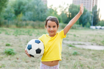 Outdoor photo of cute little girl leaning on soccer ball in green grass