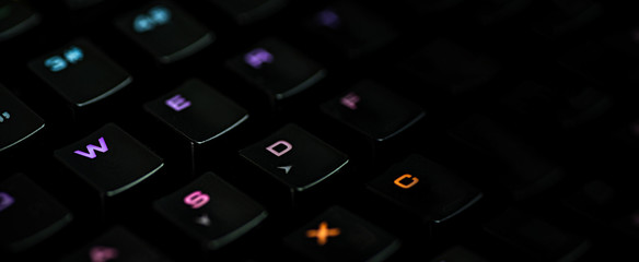 ..A gaming keyboard with rgb color backlight shot closeup on a black background with space for text. The concept of games, e-sports and the workspace of the gamer. Format banner desktop wallpaper.