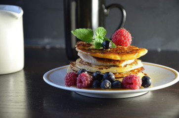 Pancakes with berries and maple syrup with raspberries and blueberries on a black background