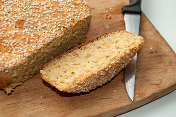 Round home gluten-free bread on a wooden board cut with a knife. Bread from corn starch, chickpeas, rice, corn flour. Bread decorated with sesame seeds.