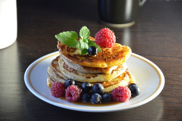 Pancakes with berries and maple syrup with raspberries and blueberries on a black background