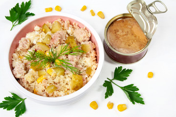 Salad with tuna, couscous, pickled cucumbers and corn, next to a can of tuna in olive oil