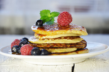 Pancakes with berries and maple syrup in a plate on a white wooden background