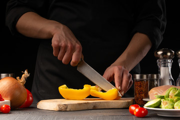 Cooking fresh salad, the chef cuts the paprika on the background of vegetables. Vegetables and healthy eating.