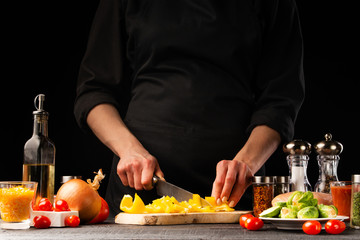 Cooking fresh salad, the chef cuts the paprika on the background of vegetables. Vegetables and healthy eating.