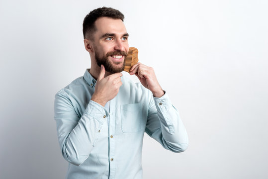 Studio shot portrait of smiling bearded man combing his beard. - Image