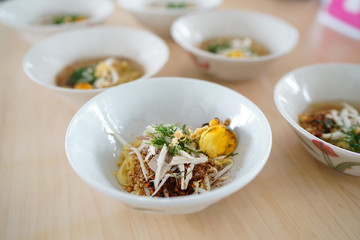 A bowl of dried noodle with chicken and boiled egg (spicy tom yum) on wooden background, Traditional Thai food recipe, Popular street food of Thailand.