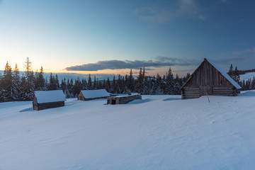 Charming snow-capped houses on a mountain Carpathian mountain valley, with magnificent views of peaks in winter.