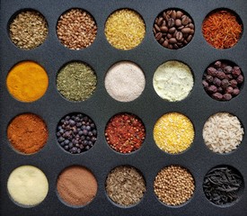 multicolored seasonings and grains in round containers on a black background