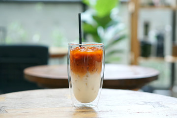 Iced milk tea - A glass of Thai tea mixed with fresh milk on table and blurred background,...