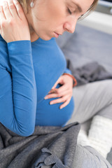 Pregnant tired exhausted woman with stomach and head issues at home on a couch, being sick.