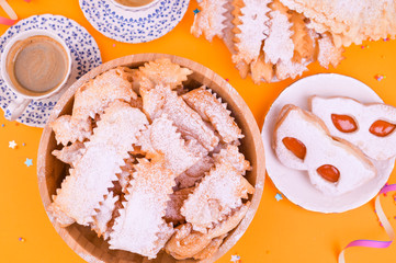Crostoli, chiacchiere, biscuit cookies and fragrant espresso on a yellow background, colored with confetti and festive decor. Coffee and sweets for a traditional Italian carnival. 