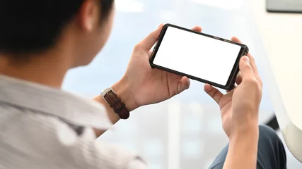 Foto op Plexiglas Creatieve man ontspannen/kijken naar een film van bijgesneden zwarte smartphone met wit leeg scherm aan de moderne werktafel als achtergrond. Ontspannen na het voltooide werkconcept. © Prathankarnpap