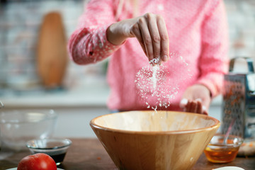 Close up of female hands putting salt in food. Woman cooking in kitchen. 