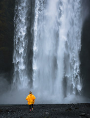 Tourist wearing a yellow raincoat walks to the Skogafoss waterfall in Iceland