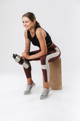 Pleased sports woman isolated over white wall background have a rest drinking water.