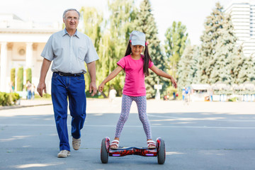 Fototapeta na wymiar Little smiling girl learning to ride a hoverboard with her parents outdoors
