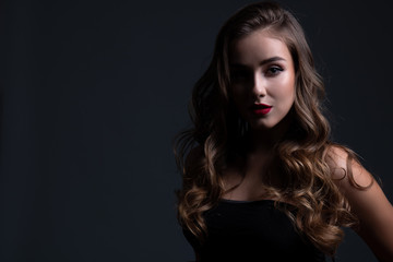 Fototapeta premium Close up beauty portrait of young beautiful girl in shadow with long curly hair wearing a black top. Text space.