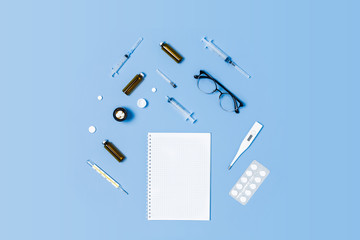 Medical blue background with different accessories: stethoscope, thermometer, syringe, tablets and notepad.