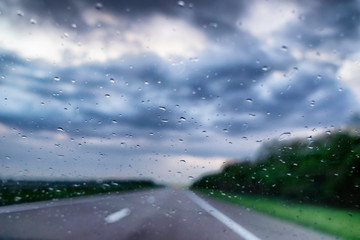 Raindrops on car windshield against a blurred highway and sky background