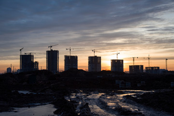 Tower cranes and building silhouette at construction site on  sunset background. Concept of the renovation program. Buildings industry.