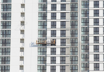 Fototapeta premium Suspended cradle on the facade of the skyscraper. Mobile scaffolding platform for construction work at height, facade cleaning, plastering, window washing, installation of window frames and glasses