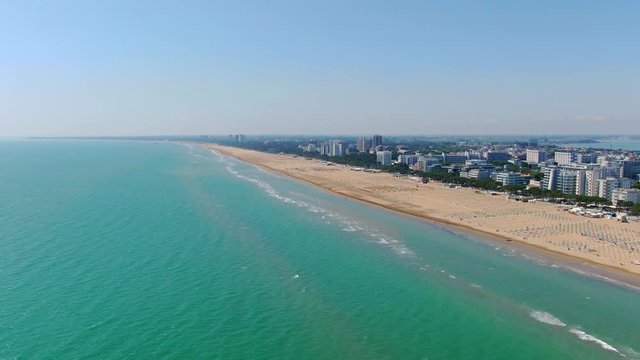 Aerial panning shot of Lignano Sabbiadoro town and Adriatic sea turquoise color water