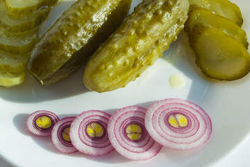 pickled cucumbers on a white plate next to onion rings. homemade vegetables for a healthy diet. close-up, top view.