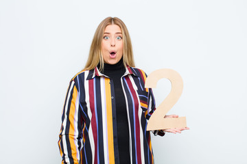 young pretty blonde woman surprised, shocked, amazed, holding a number 2.