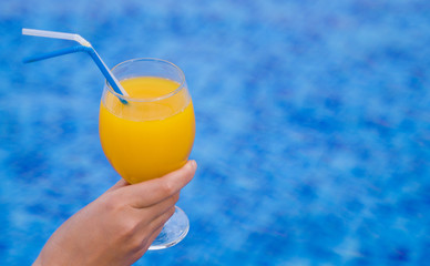 Woman sitting near the pool and holding glass with orange juice.
