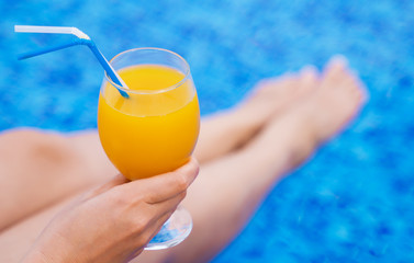 Woman sitting near the pool and holding glass with orange juice.