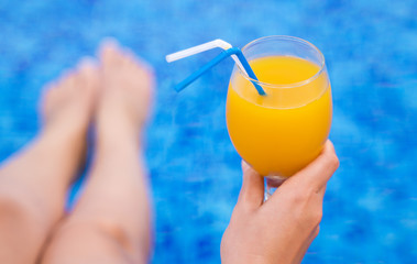 Woman sitting near the pool and holding glass with orange juice.