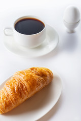 Breakfast. Croissant, coffee and soft-boiled egg. High key. Selective focus.