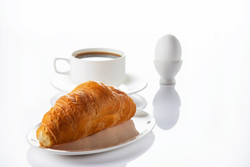 Breakfast. Croissant, coffee and soft-boiled egg. High key.  Selective focus.